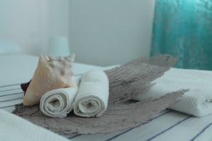 A neatly made bed with a striped bedspread, two rolled white towels, and a decorative shell. - B&B Villa Luna (San Rafael del Yuma)