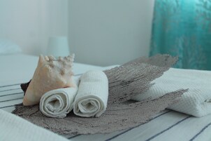 A neatly made bed with a striped bedspread, two rolled white towels, and a decorative shell.
