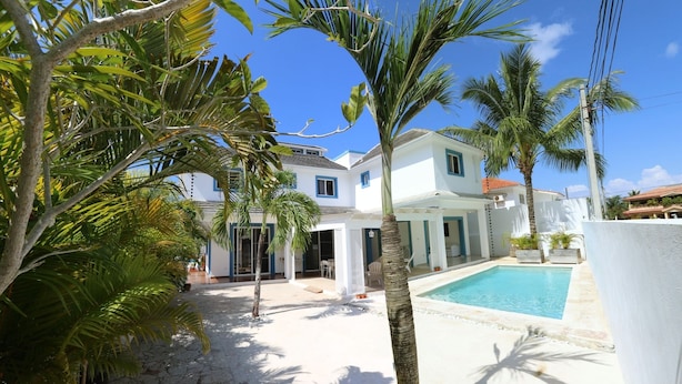 Eine weiße Villa mit Pool, umgeben von Palmen und wolkenlosem, blauem Himmel.