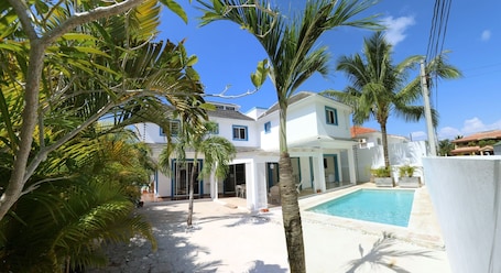A white villa with a pool, surrounded by palm trees and a clear blue sky.