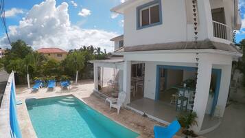 Ein zweistöckiges Haus mit Swimmingpool, Sitzgelegenheiten im Freien und einer überdachten Terrasse.