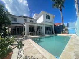 A two-story house with a swimming pool, outdoor seating area, and potted plants.