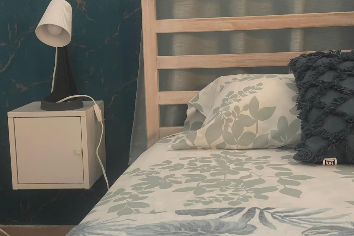 Une chambre à coucher comprenant un lit, une table de chevet, une lampe et un mur orné d’un motif de feuilles.