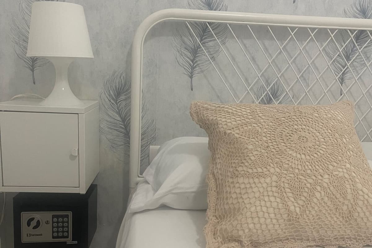 Un lit bien fait, agrémenté d’un oreiller à texture intéressante, une table de chevet blanche avec une lampe, et une petite table de nuit dotée d’un panneau de commande.