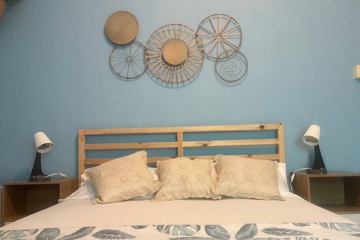 Une chambre à coucher avec une tête de lit en bois, une couvre-lit à motifs floraux et un objet décoratif fixé au mur au-dessus du lit.