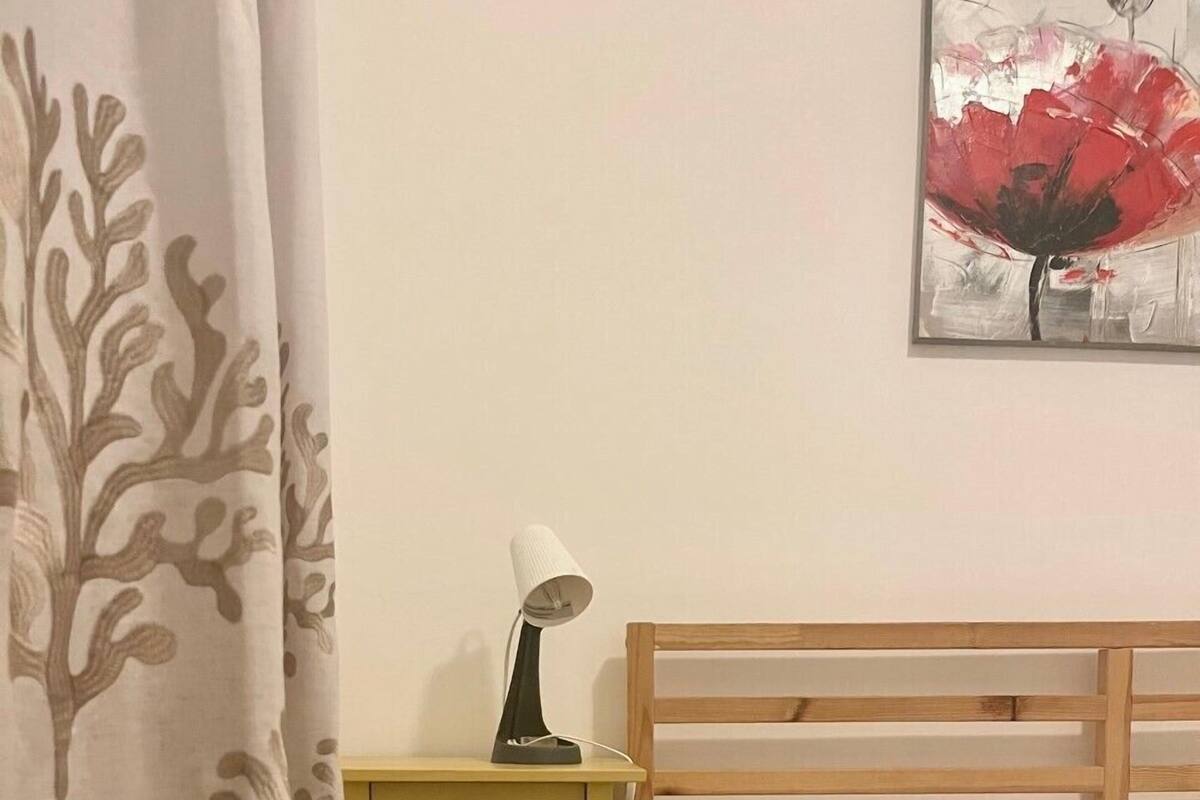 Une chambre à coucher avec un lit en bois, du linge de lit blanc, une table de chevet avec une lampe et un tableau accroché au mur.