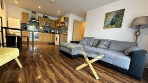Una sala de estar moderna con un sofá gris, suelo de madera y una mesa de centro de cristal.