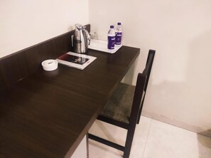 Una kitchenette pequeña con cafetera, hervidor de agua y botellas de agua sobre la encimera.