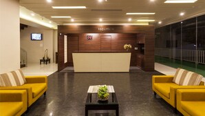 A reception area with a reception desk, two yellow sofas, a coffee table with a plant, and a TV on the wall. - Hotel Rasika (Kolhapur)