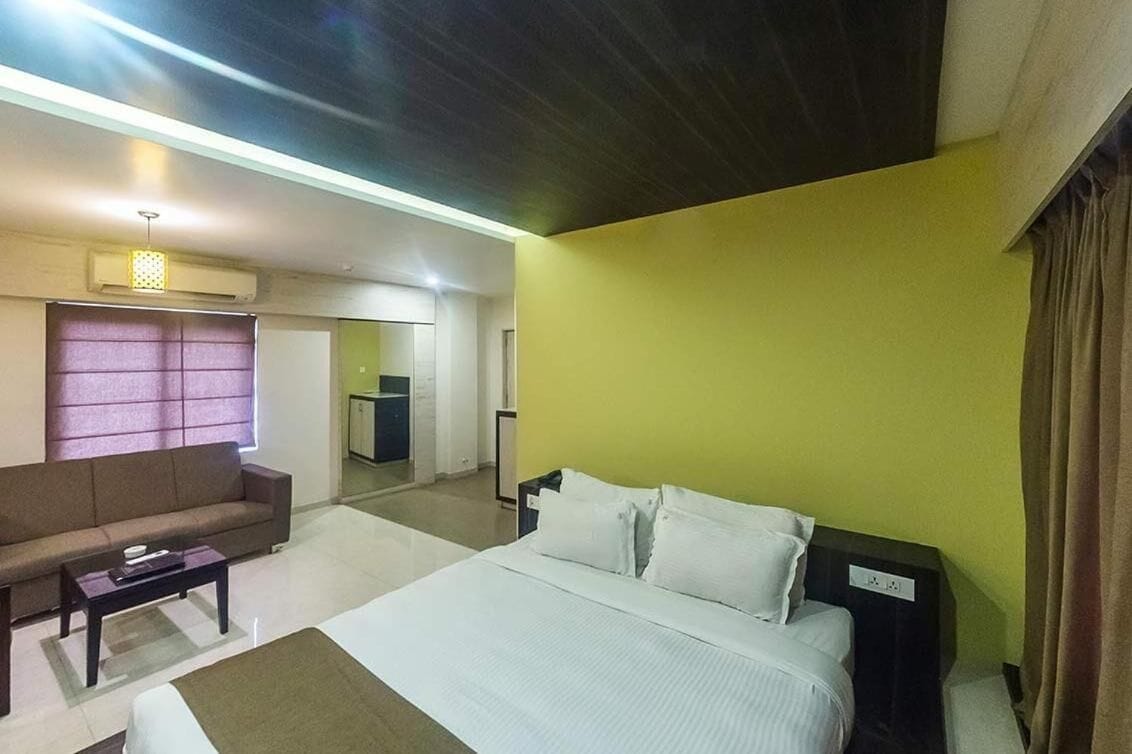 A hotel room with a bed, a sofa, a small table, and a mirror.