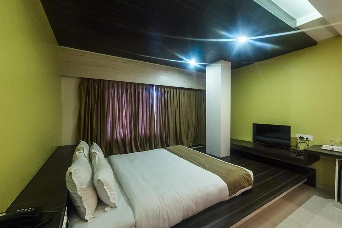 A modern hotel room with a large bed, a desk with a TV, and a window with curtains.