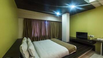 A modern hotel room with a large bed, a desk with a TV, and a window with curtains.