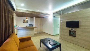 A modern living room with a sofa, a coffee table, a TV mounted on the wall, and a kitchen area in the background. - Hotel Rasika (Kolhapur)