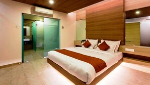 A modern hotel room with a large bed, a wooden headboard, a bedside table, and a large mirror. - Hotel Rasika (Kolhapur)