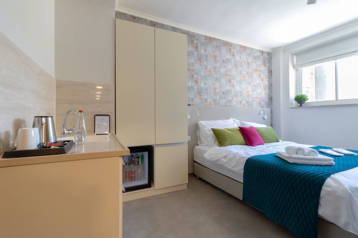 A bedroom with a bed, a bedside table, a wardrobe, a window, and a small plant.