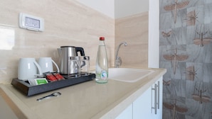 Una cocina con cafetera, una botella y una bandeja con tazas y condimentos.