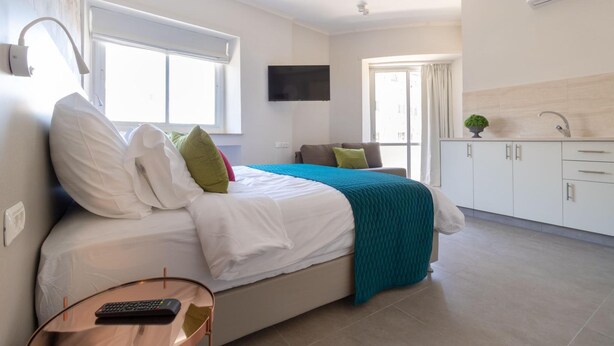 Una habitación de hotel moderna con cama, televisor, una mesita y una kitchenette.