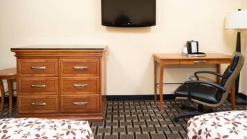 A hotel room with a wooden dresser, a desk with a chair, a television, and a patterned bedspread.