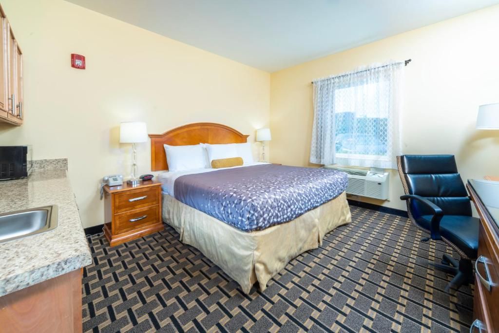 A hotel room with a bed, bedside tables, a desk, a chair, a window with curtains, and a patterned floor.