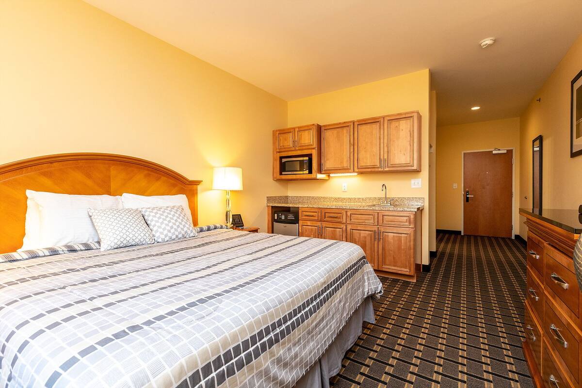 A hotel room with a large bed, wooden cabinets, a microwave, and a small kitchenette.
