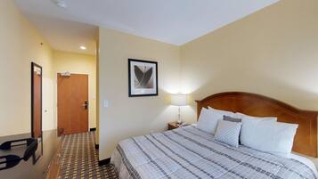 Una habitación de hotel con una cama, una lámpara de noche, un cuadro en la pared y una puerta.