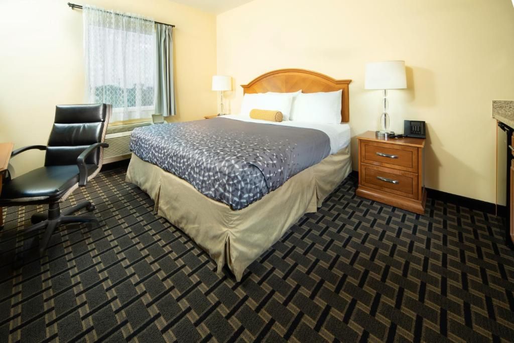 A hotel room with a bed, a desk, a chair, a nightstand, and a window with curtains.