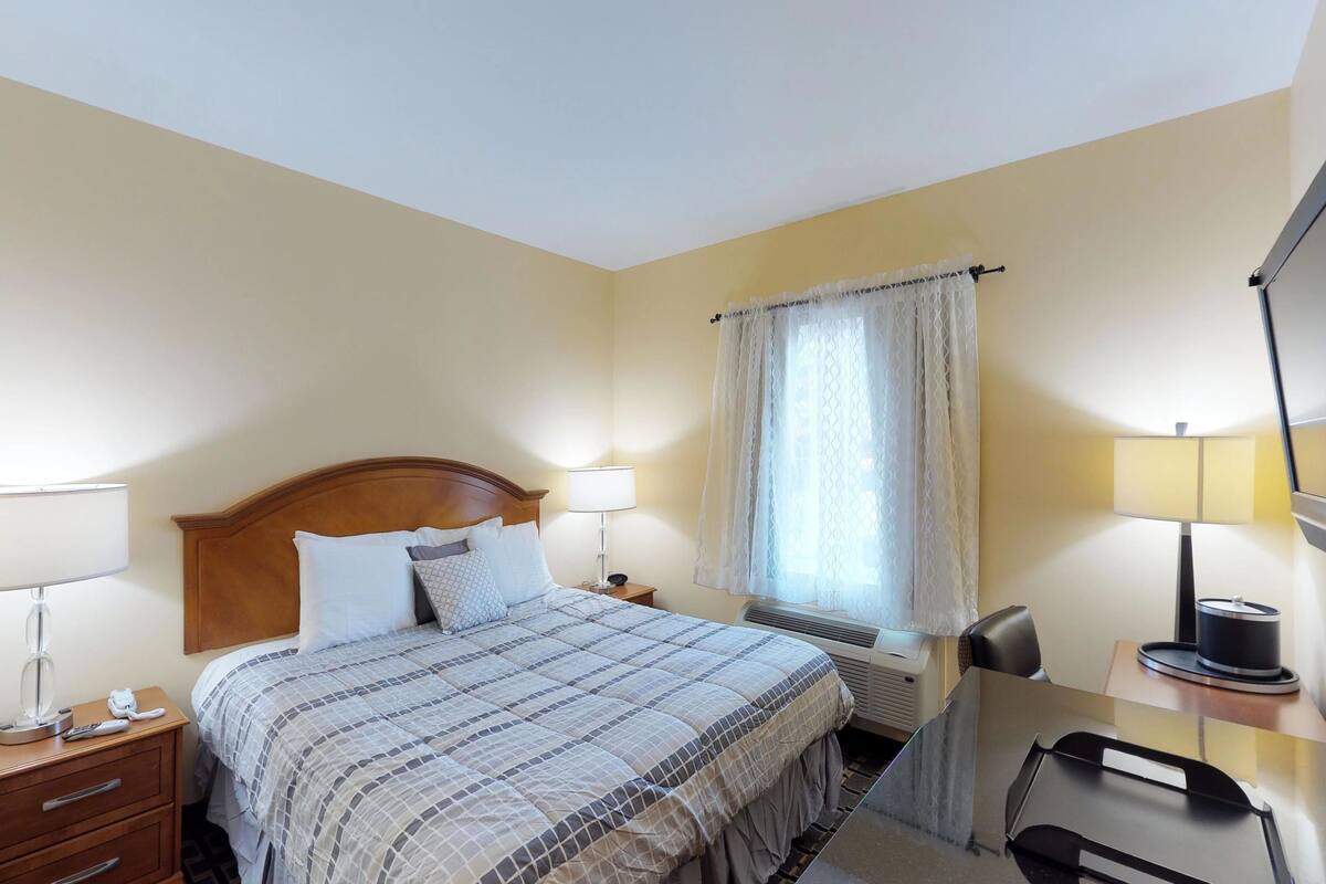 A hotel room with a bed, bedside lamps, a desk with a chair, a TV, and a window with curtains.
