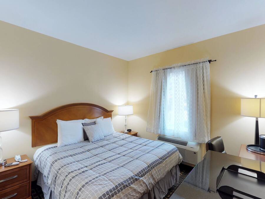 A hotel room with a bed, bedside lamps, a desk with a chair, a TV, and a window with curtains.