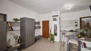 A modern living room with a dining area, a kitchen, and a bathroom. There are bookshelves, a bench, and a potted plant. - Bed & Breakfast L'aquilino (Iglesias)
