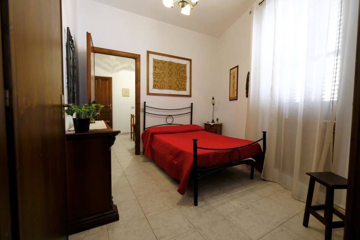 Un dormitorio con cama, cómoda de madera, espejo y puerta que da a otra habitación.