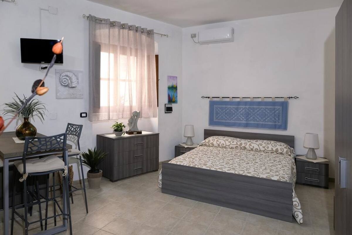 Un dormitorio con cama, mesitas de noche, un escritorio con silla, televisor y ventana con cortinas.