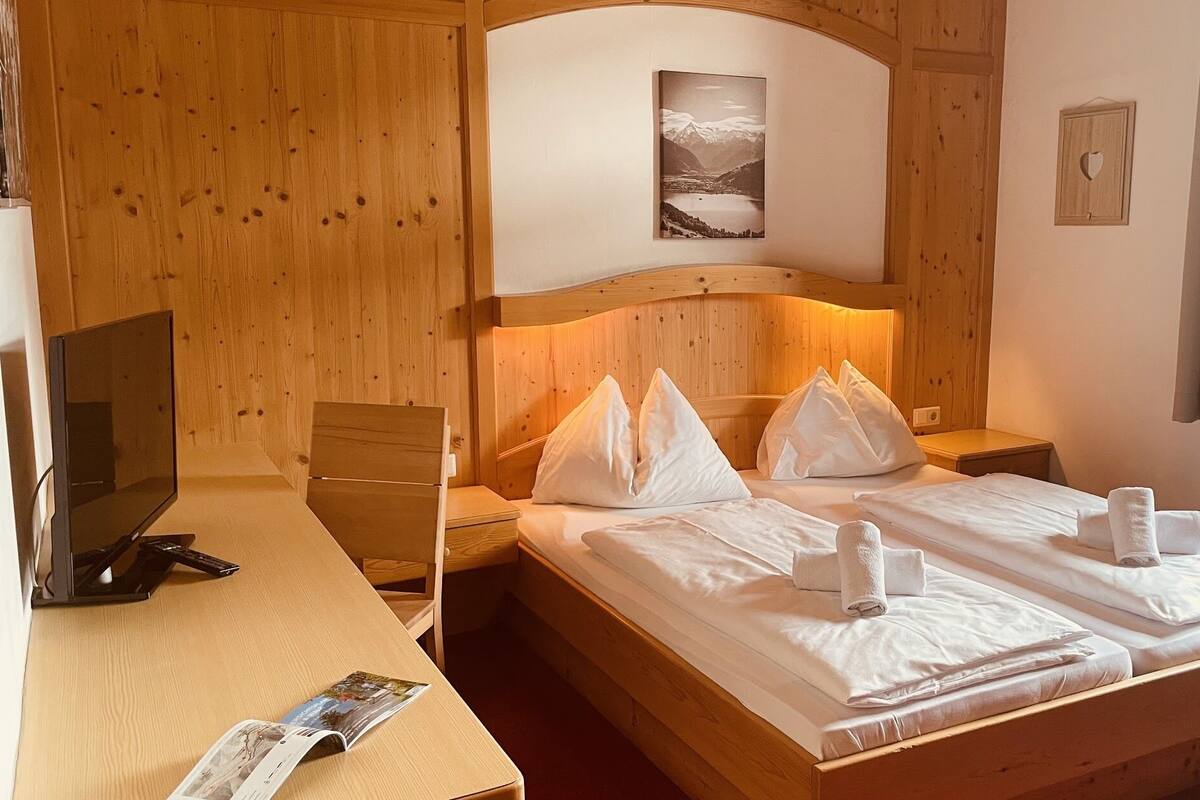 A hotel room with a wooden headboard, a bed with white linens and pillows, a bedside table with a lamp, a TV, and a magazine on the table.