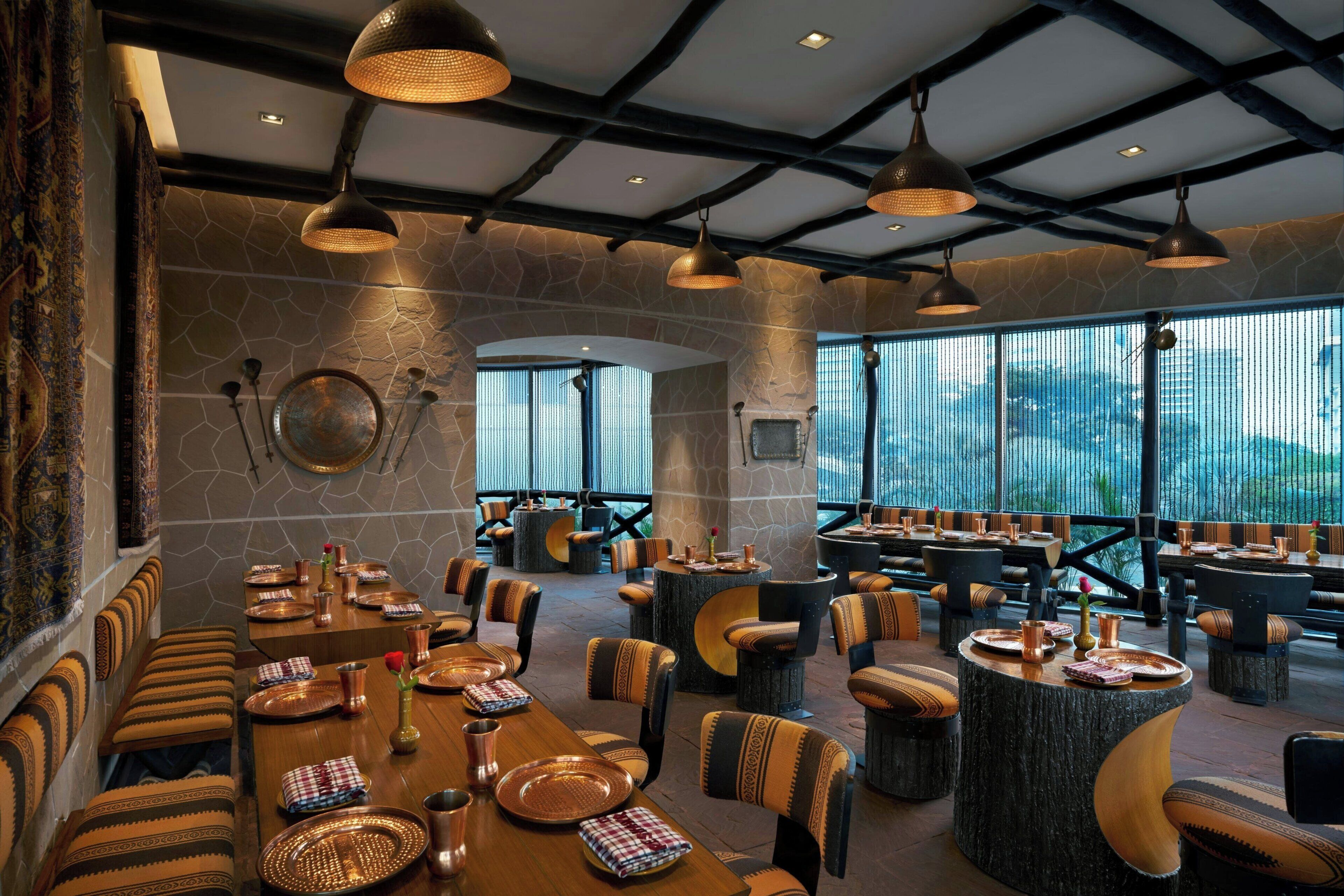 A spacious dining area with multiple tables and chairs, large windows offering a view, and a high ceiling with exposed beams.