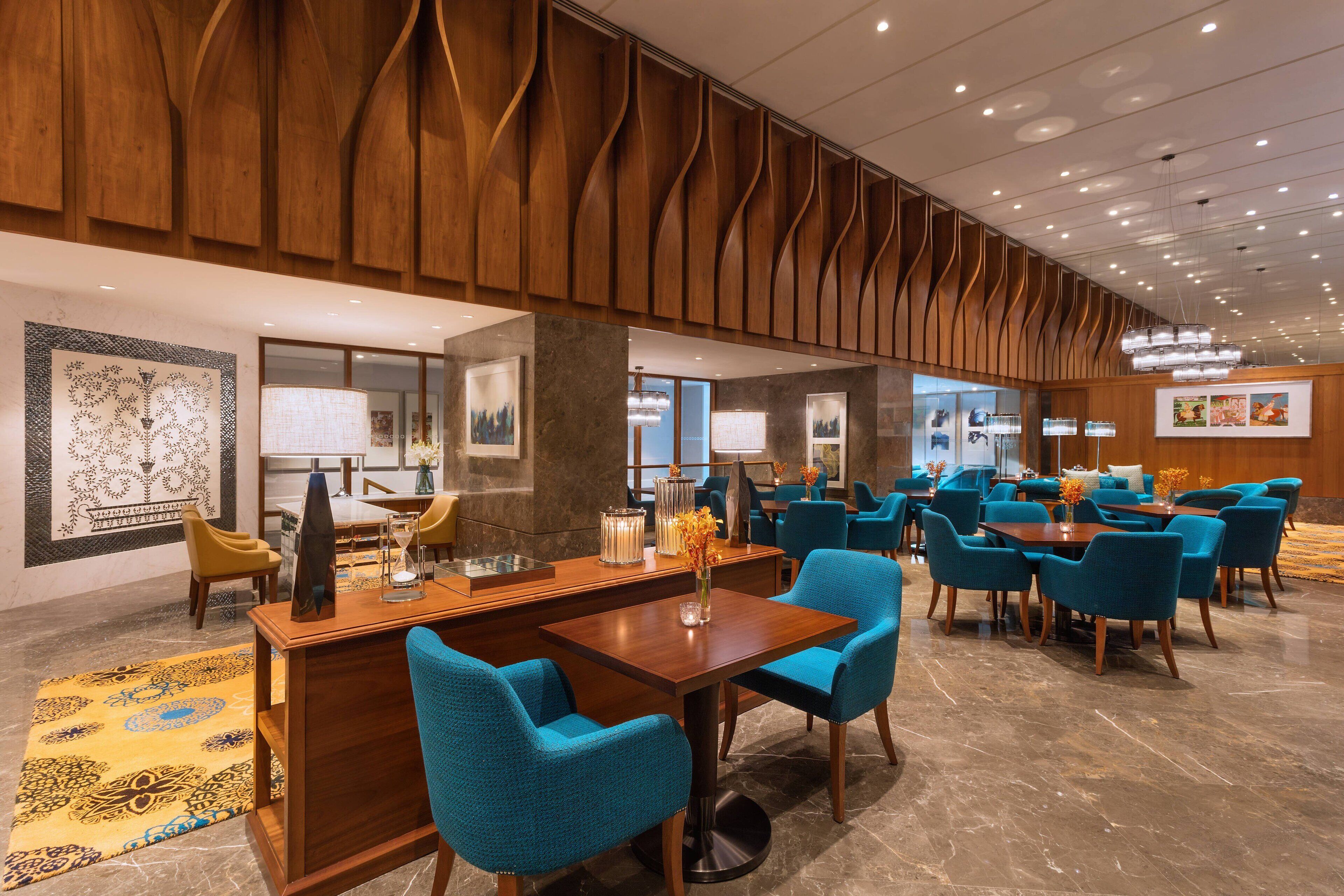 A modern hotel lobby with wooden paneling, a reception desk, and blue upholstered chairs.