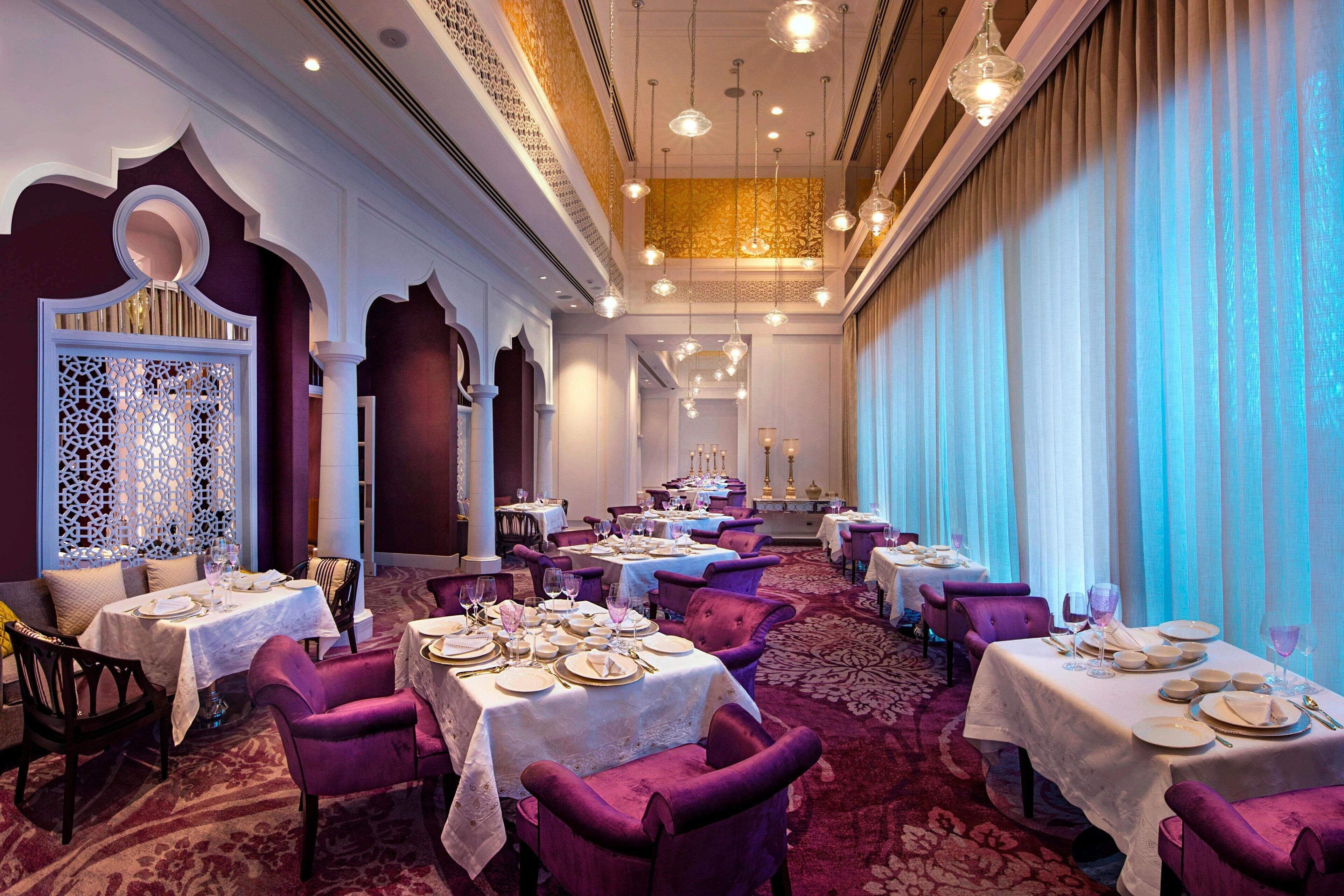 A formal dining room with tables set for service, ornate architectural details, and a patterned carpet.