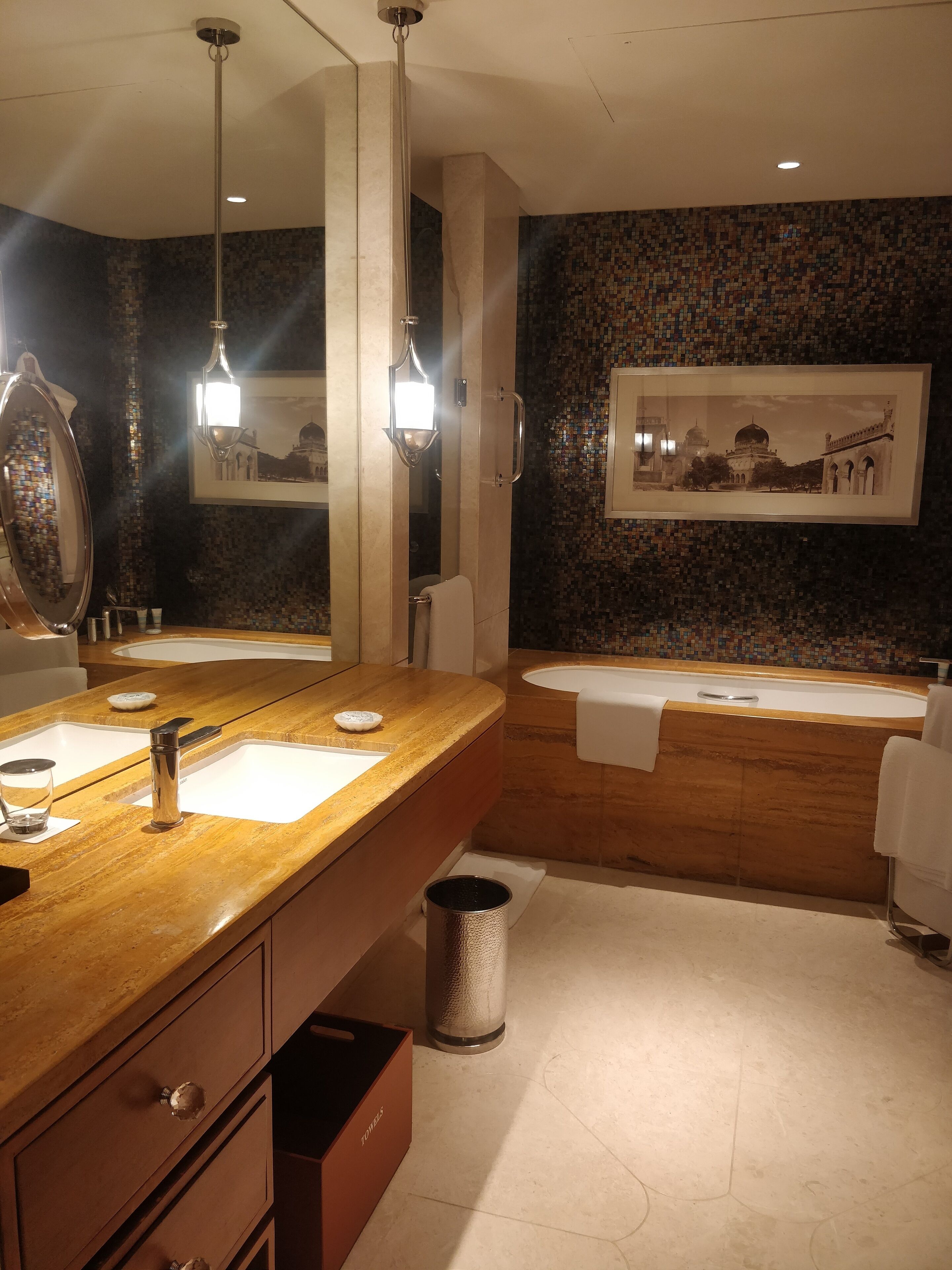 A modern bathroom with a large mirror, two sinks, a bathtub, and a toilet.