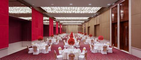 Un salón de banquetes con mesas redondas, manteles blancos y centros de mesa florales rojos.