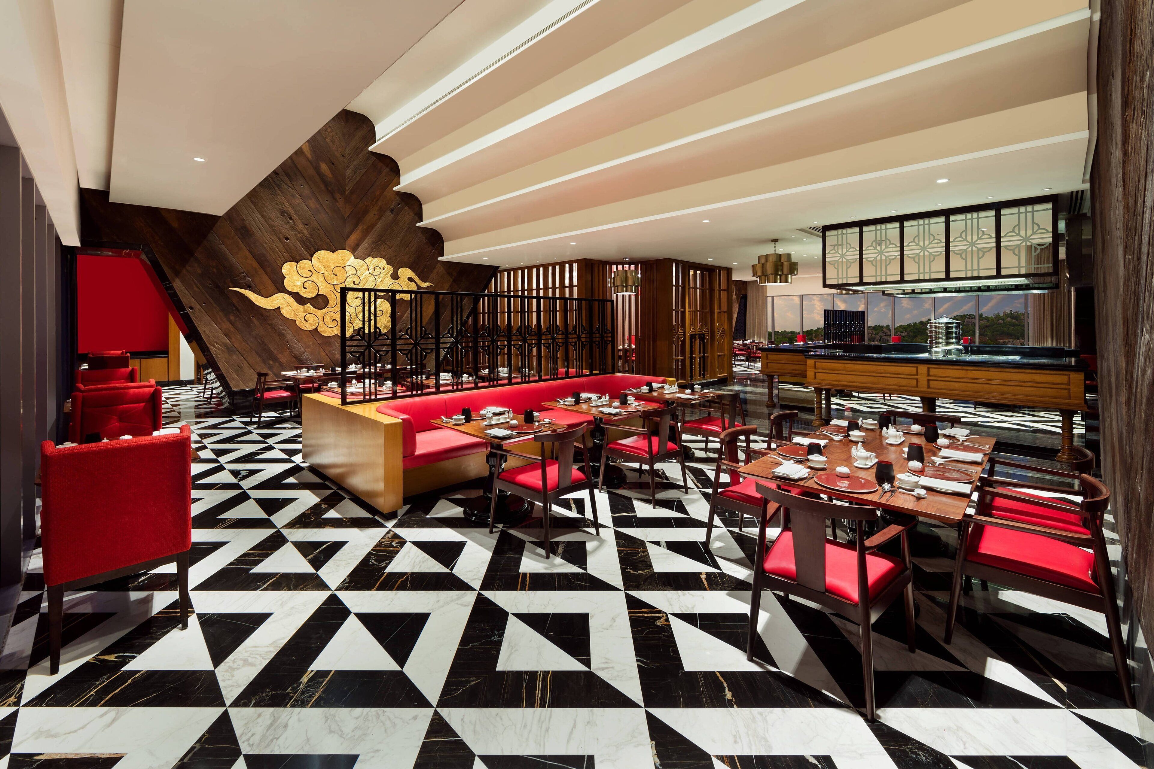 A restaurant with a black and white checkered floor, red seating, and a wooden accent wall with a golden design.