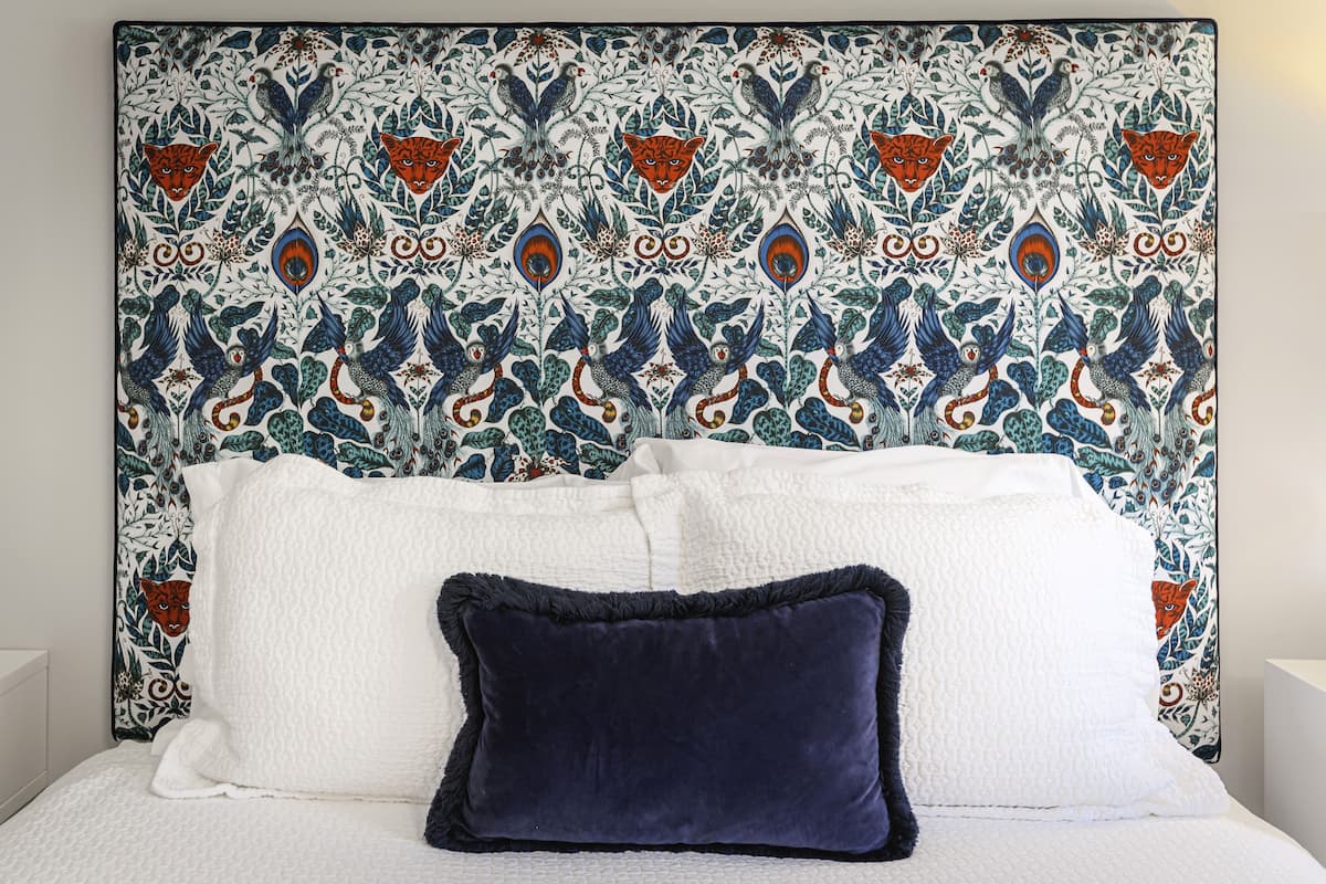 A bed with white and dark blue pillows, a patterned headboard, and a white wall.