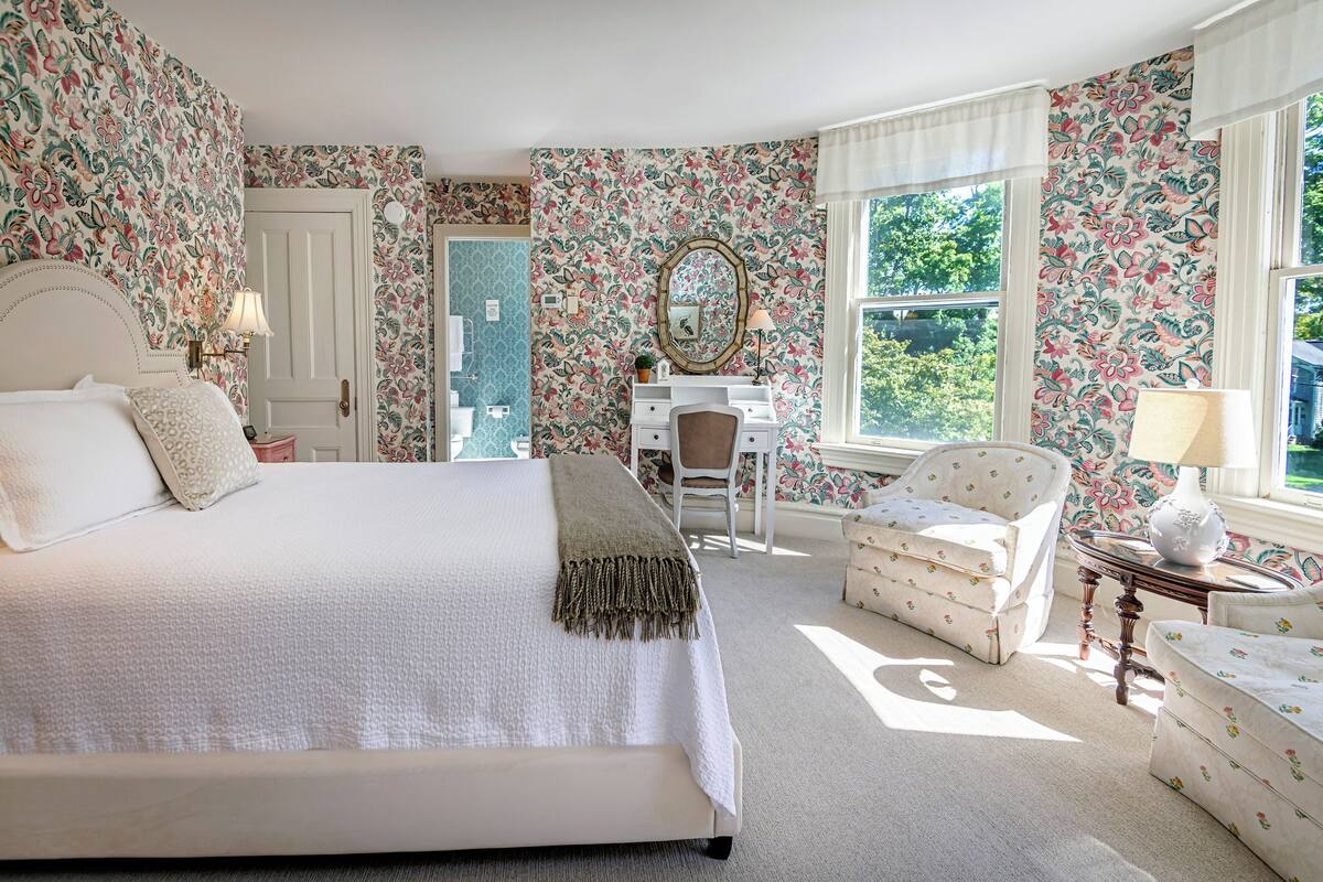 A bedroom with a large bed, a desk, a chair, and a window.
