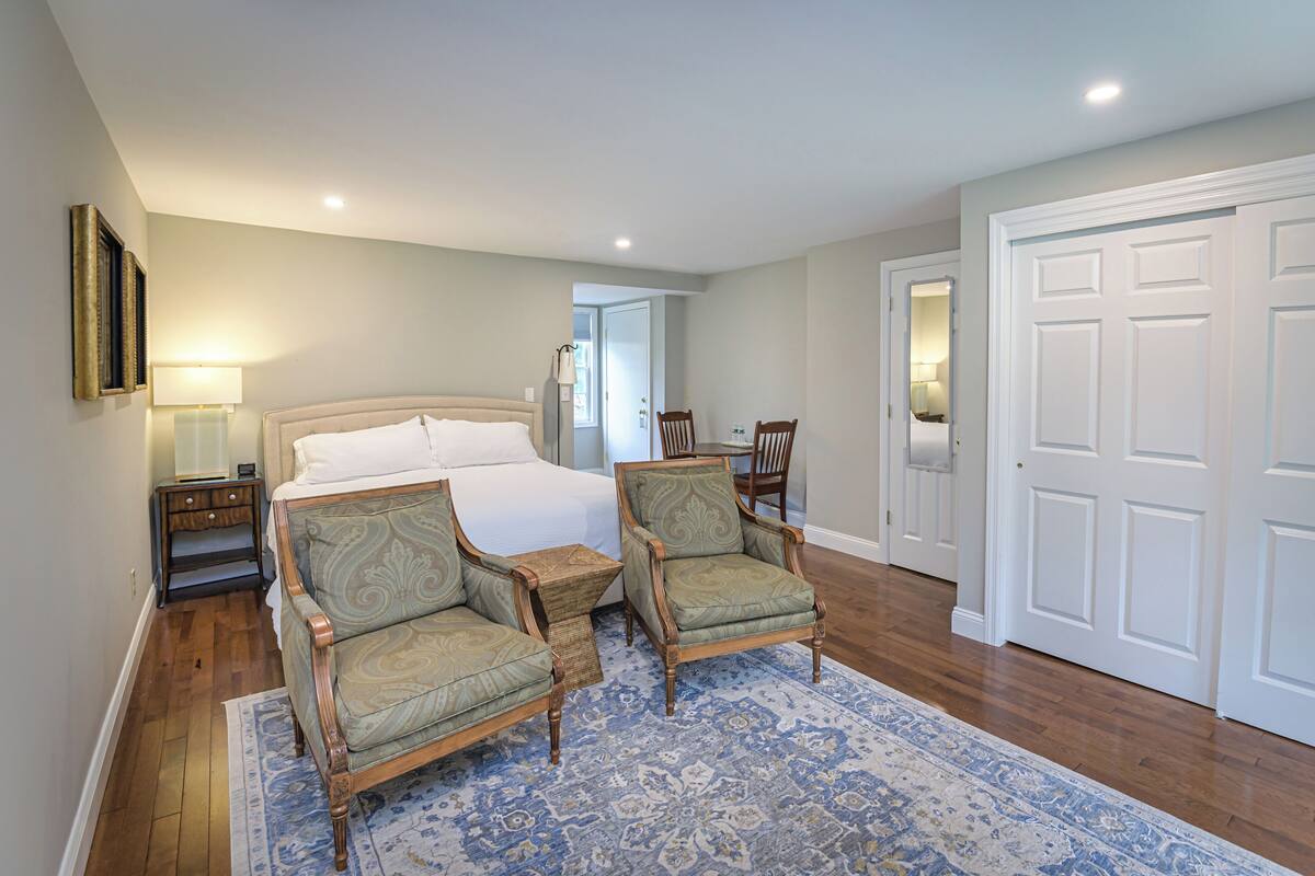 A bedroom with a bed, two armchairs, a nightstand, a lamp, and a door.