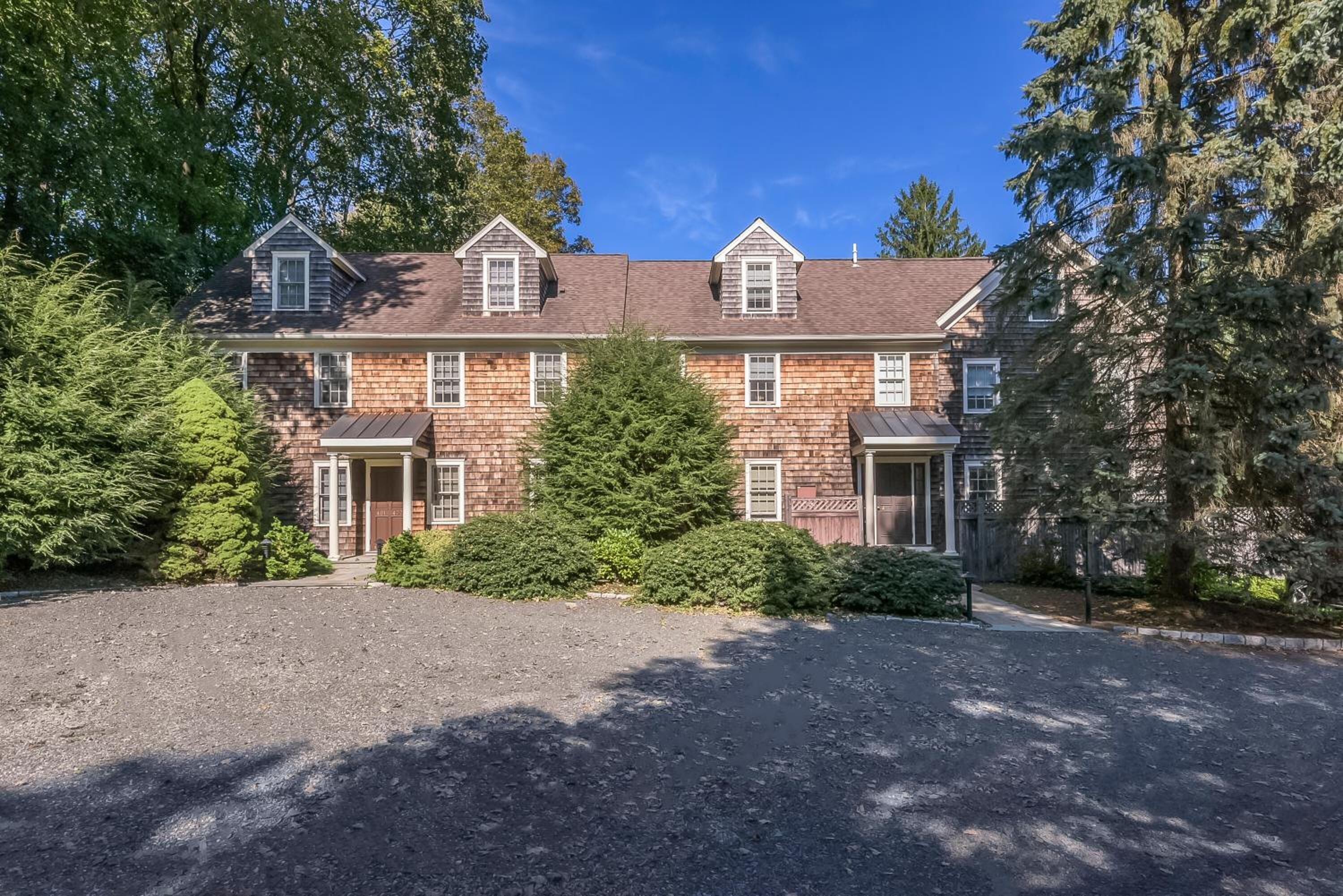 A two-story brick house with a gravel driveway and a large evergreen tree in front.