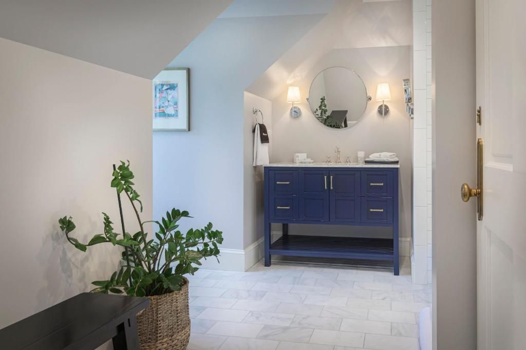 A bathroom with a dark blue vanity, a round mirror, and a wall-mounted light fixture.