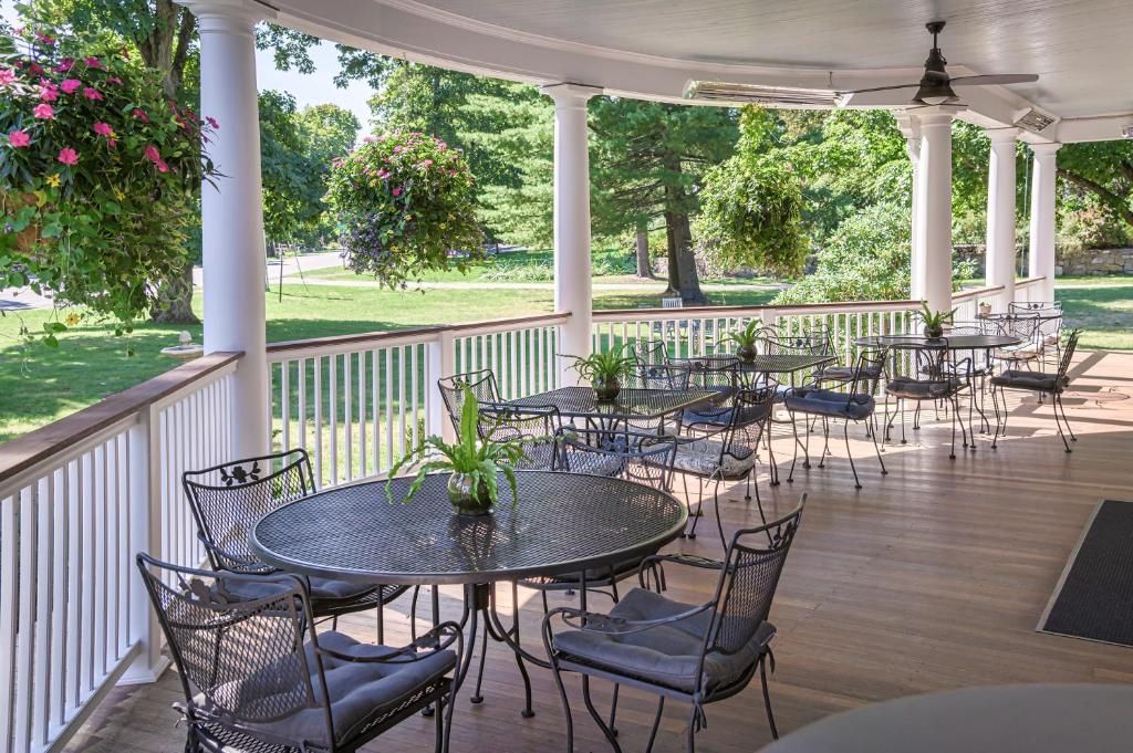 Une terrasse extérieure couverte, dotée de tables et de chaises rondes, entourée de colonnes blanches et offrant une vue sur une pelouse bien entretenue et des arbres.