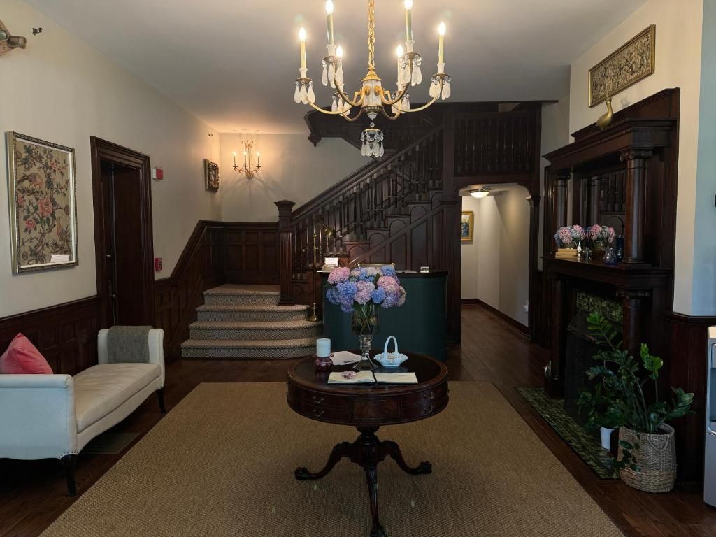 Un'imponente scala conduce a un piano superiore, con un lampadario, un tavolo rotondo con un vaso di fiori e un divano in un'ampia zona di accoglienza.
