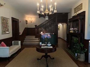 A grand staircase leading to an upper floor, a chandelier, a round table with a vase of flowers, and a sofa in a spacious lobby area. - West Lane Inn (Ridgefield)