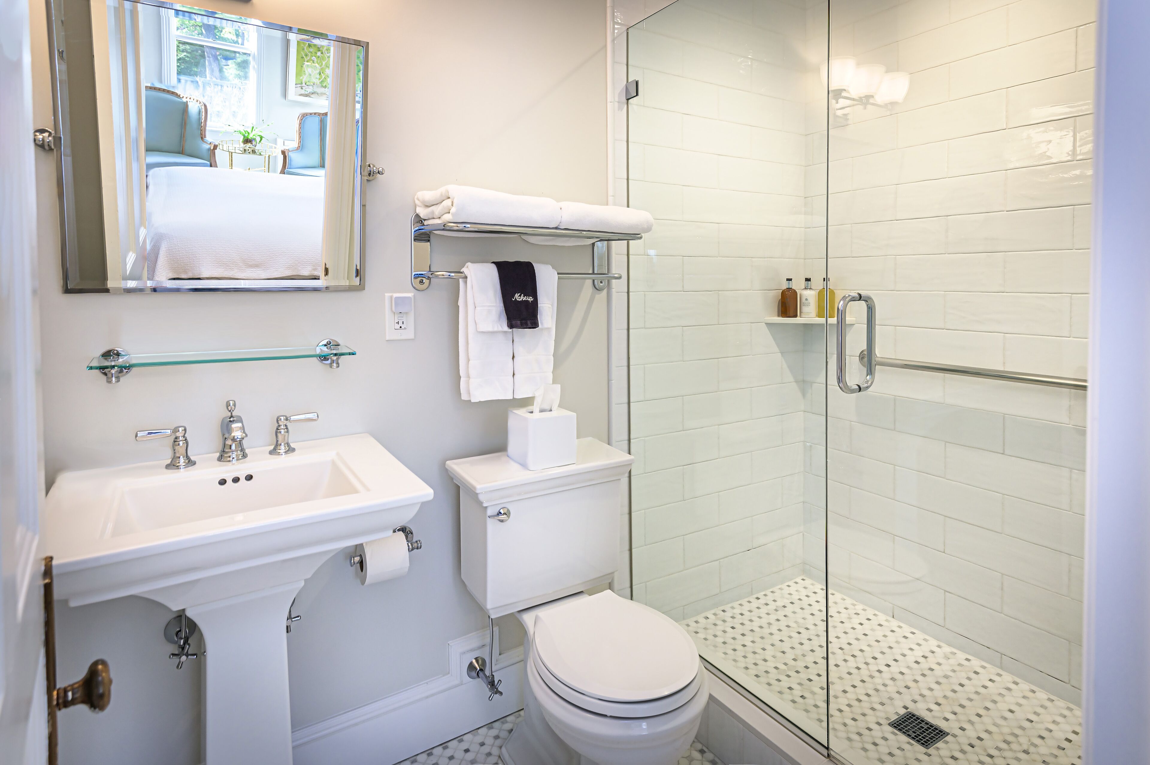 A modern bathroom with a glass shower enclosure, a white sink with a glass shelf, and a toilet with a towel rack above.