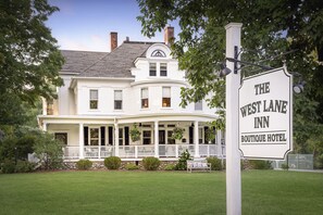 A large, white, two-story building with a curved front porch and a sign that reads "The West Lane Inn Boutique Hotel."