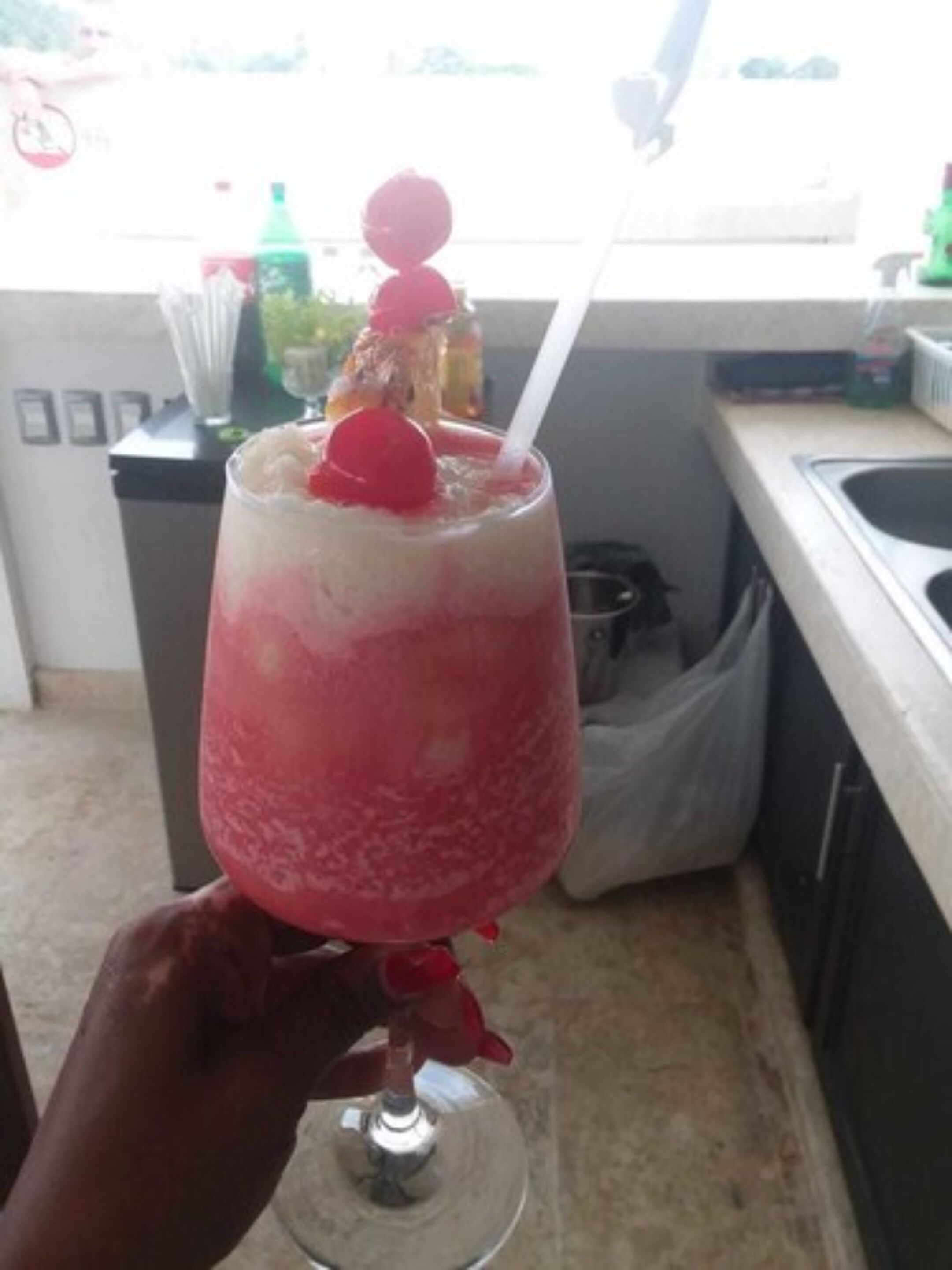 Un cocktail servi dans un verre, garni d’une cerise, tenu dans une main.