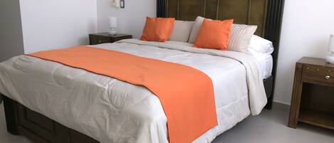 A bed with a wooden headboard, white and orange bedding, and a nightstand with a lamp.
